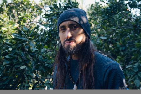 Portrait, adult Latino man, he is resting in the shadows of the tree on the farm, standing next to...