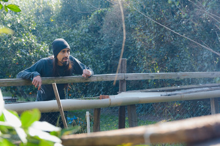 Man in the garden leaning on the wooden railing, he is watching the harvest from outside, thinking about going to harvest the vegetables, farm concept, copy spaceの写真素材