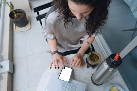 top view Caucasian Woman with curlers sitting on balcony using smartphone, blank screen, copy space,...