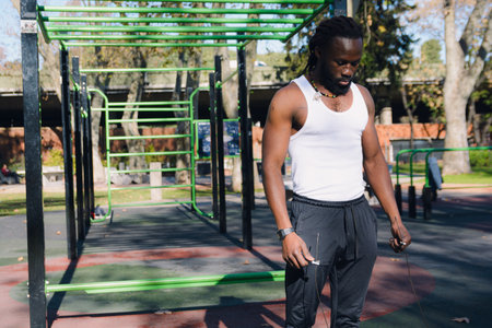 Young Man of African ethnicity, standing in the park resting after a jump rope session, he is...