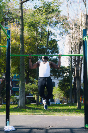 Vertical image of strong African black man doing pull ups, calisthenics exercise in the park, there...