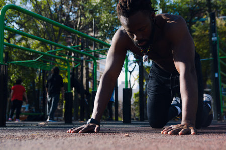 Black man with dreadlocks is kneeling on the ground, training and resting after a push-up routineの写真素材