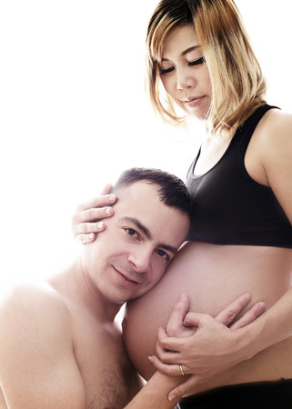 Beautiful future parents: his pregnant asian wife and a happy husband acting kiss togetherの写真素材