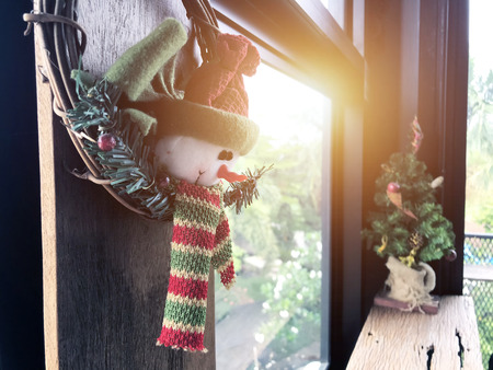 Snowman doll christmas ornament or decoration hanging on the window home living room with christmas tree and ray of morning sun. Merry xmas day background.の写真素材