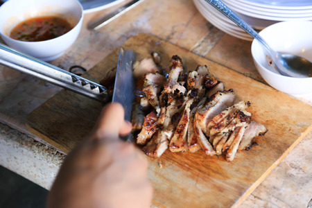 Hand holding knife cutting barbecue pork grilled slices on wood plate.の写真素材