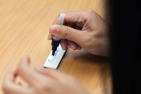 Close-up hand holding buffer and drop mucus sample placed on strip of Antigen test kit (ATK) for...