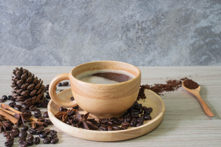 Black hot coffee in wooden cup and wooden spoon with cinnamon, pumpkins and star anise and coffee beans and on wooden backgroundの写真素材
