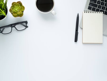 Workplace in office with white desk. Top view from above of laptop with notepad and coffee. Space for modern creative work of designer. Flat lay with blank copy space. Business and finance concept.の写真素材
