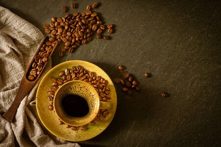 Close-up of Black hot coffee for morning with milk foam in brown ceramic cup and napkin with coffee beans roasted in sack on dark table stone background. Top view, flat lay with copy space.の写真素材