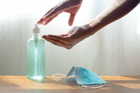 Close-up of man hand pressing the hand sanitizer gel with medical mask on table. Prevention of...