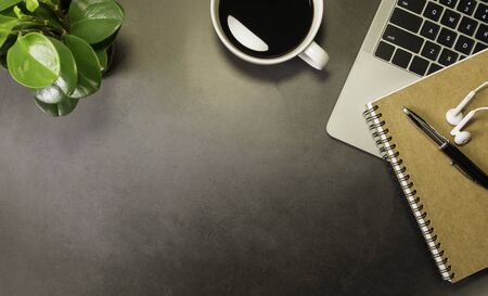 Workplace in office with dark grey table. Top view above of laptop with notebook, earphone and...