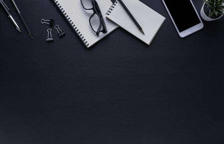 Workplace office with dark black desk. Top view from above of Empty open notebook, phone with glasses and pencil with paper clip. Flat lay, Business-finance or education concept with copy space.の写真素材