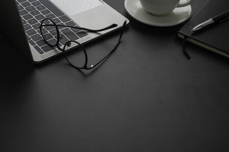 Close-up view from above of laptop, glasses with notebook and cup coffee. Workplace office with dark...
