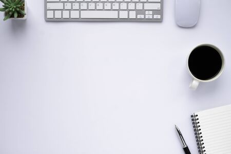Workspace in office with white table. Top view from above of keyboard with notebook and coffee. Desk for modern creative work of designer. Flat lay with blank copy space. Business and finance concept.の写真素材