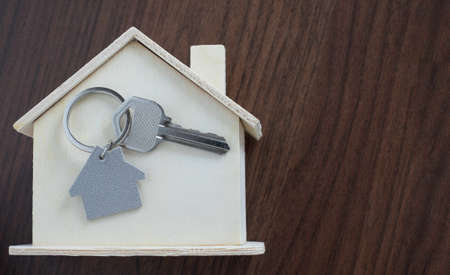 Close-up of Silver key house with house shaped keychain and home mock-up on wooden table background. Real estate concept for buying a new home with copy space.の写真素材