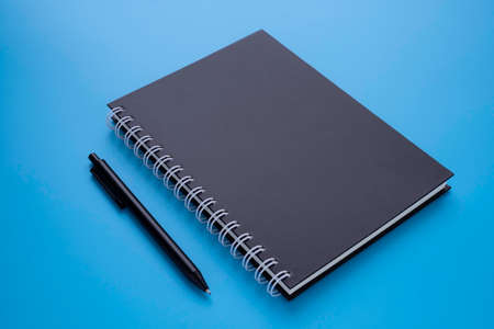 Black spiral notebook with pen isolated on blue background for design a mockup. Education and...