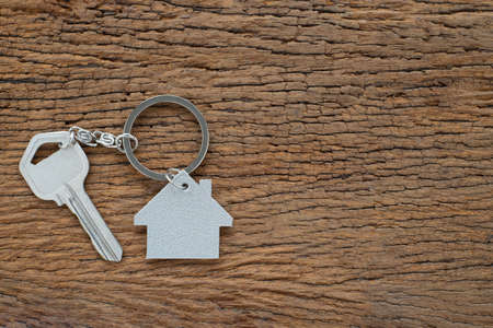 Silver key house with house shaped keychain on vintage wooden table background. Real estate concept...