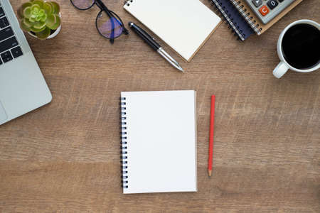 Top view above of Notebook on wood office desk table with laptop and coffee cup with equipment other...