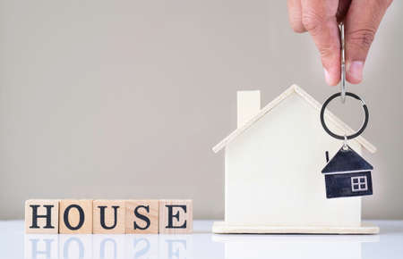 Close-up of Hand holding silver keys house with house shaped keychain and home mockup on white table...