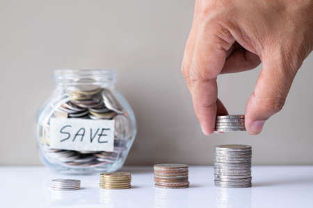 Business investment and finance accounting concept. Hand putting coin into stack step up growing growth with coins in glass bottle. Saving money with empty copy free space.の写真素材