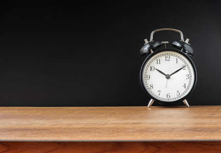 Retro alarm black clock vintage style on wooden table a black wall background with copy space.