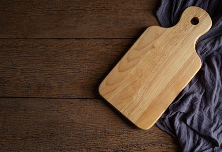 Top view above of Wooden chopping board with apron on wood table background. Empty wood cutting board with handle and hole for hanging with copy space.の写真素材