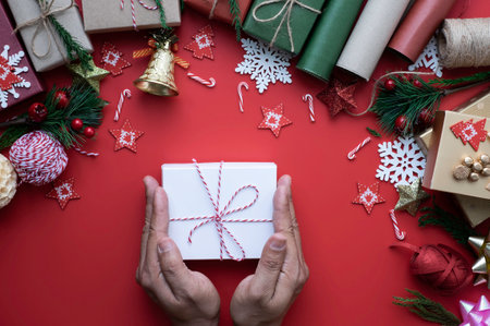 Hand with white gift box, christmas holiday on red background. Composition with fir pine branches,...