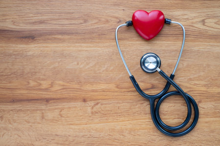 Black stethoscope with red heart of doctor for checkup on wood table background. Stethoscope equipment of medical use to diagnose hear sound. Health care and cardiology concept with copy space.の写真素材