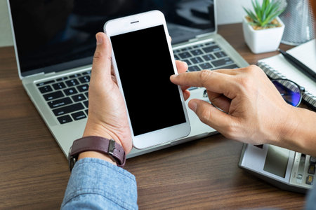 Close-up shot of Businessman hands using, holding smartphone or mobile mockup with blank screen display at office desk. Phone technology, digital modern design can use touch screen with copy space.の写真素材