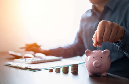 Shot of man hand putting coins in pink piggy bank with money stack step up growing growth. Planning step up, saving money for future plan, retirement fund. Business investment-finance account concept.の写真素材