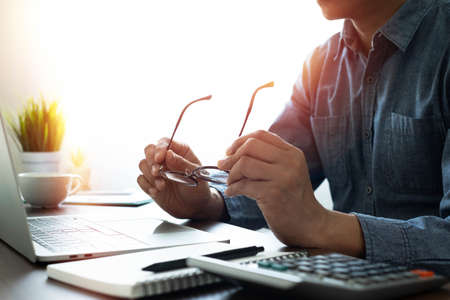 shot of Glasses in hands businessman freelancer using for work business with laptop computer on desk table in office with copy space. Business investment-finance accounting concept.の写真素材