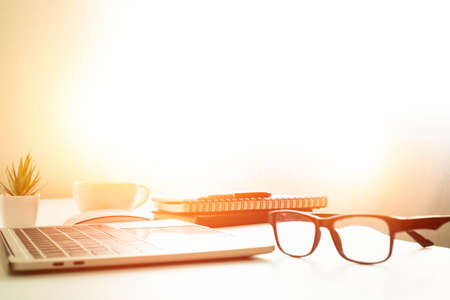 soft focus of Office desk table with keyboard of laptop computer, coffee cup and notebook, glasses. Business and finance concept. Workplace with morning sunlight from window with copy space.の写真素材