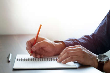 Close-up of man hand using writing pencil memo on notebook paper or letter, diary on table desk...