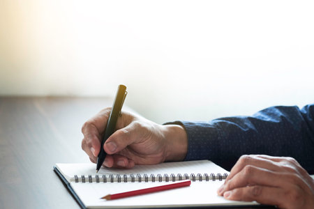 Businessman hand holding writing pen memo into notebook paper on table desk office. Workplace for business and student, writer with copy space. business working and learning education concept.の写真素材