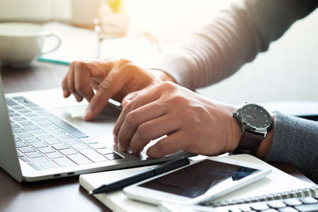 Close-up shot of man's hand with watch on his wrist. using keyboard of laptop computer on office desk. businessman working in office. Business investment-finance accounting concept.の写真素材