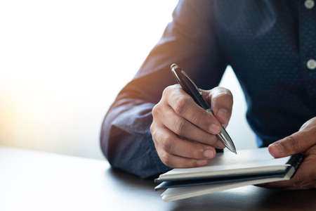 Businessman hand holding writing pen memo into notebook paper on table desk office. Workplace for business and student, writer with copy space. business working and learning education concept.の写真素材