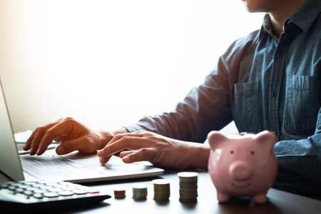 Close-up shot of man's hand using keyboard of laptop computer with money stack step up growing growth on office desk. Planning step up, saving money. Business investment-finance accounting concept.の写真素材