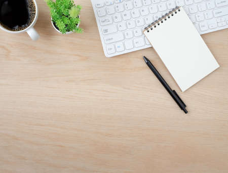 Top view above of Wood office desk table with keyboard, notebook and notepad, coffee cup with...
