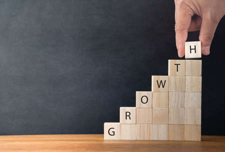 Hand arranging wood cube block with word GROWTH stacking as step-up stair on wooden table...