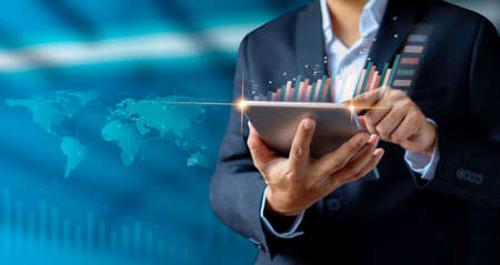 Businessman holding tablet with showing a growing hologram stock, analyzing sales data and economic growth plan graph chart success. Business finance and marketing digital technology concept.の写真素材