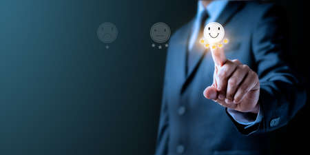 Customer service and Experience satisfaction evaluation concept. Image of Businessman hand chooses pressing smiley face emotion on virtual touch screen. Best services rating client pressing five star.の写真素材