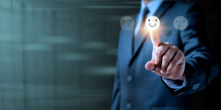 Customer service and Experience satisfaction evaluation concept. Image of Businessman hand chooses pressing smiley face emotion on virtual touch screen. Best services rating client.の写真素材