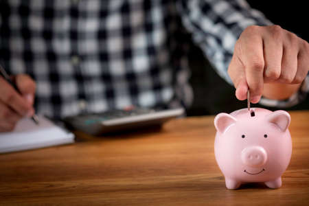 A man hand putting coins in pink piggy bank for account save money. Planning step up, saving money...