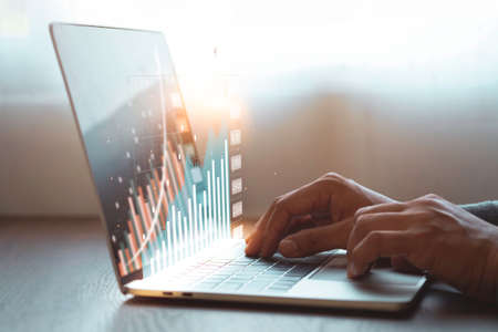 A man hand using and typing keyboard of laptop computer analyzing sales data and economic growth plan graph chart success. Business finance and marketing digital technology concept.の写真素材