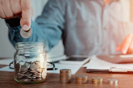 Shot of man hand putting coins in glass bottle bank with money stack step up growth. Planning step up, saving money for future plan, retirement fund. Business investment-finance account concept.の写真素材