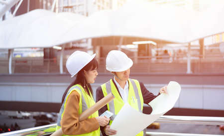 Asian civil engineer, Building Architect, inspector, contractor, wearing safety helmet. Colleagues, discussing survey with blueprint about construction building project on site. Engineering concept.の写真素材