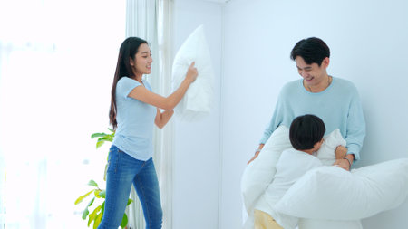 Happy family time, Young asian mother and father are playing fight pillow together with son on bed...