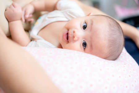 Happy family Cute Asian newborn lies in mom's lap looking at camera with smile. While your mother...