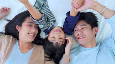 Happy family time, Top view of Asian young mother, father and children boy laying together on bed in bedroom with happy and laughing smile. Weekend time parenting with love good time relaxing at home.の写真素材