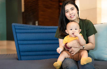 Happy family, Cute Asian newborn baby with young mother smile happy face sitting sofa at home....